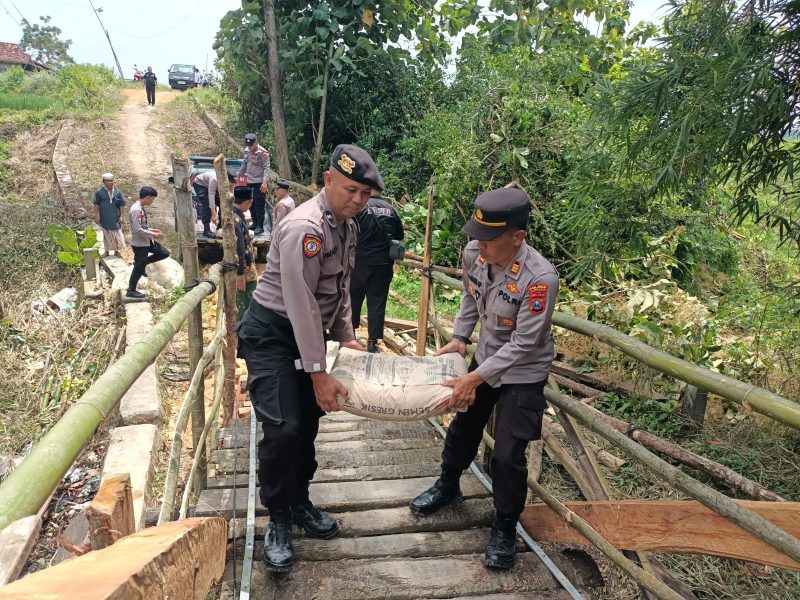 Personil Polres Pamekasan tengah mengangkat semen untuk membantu pembangunan jembatan.